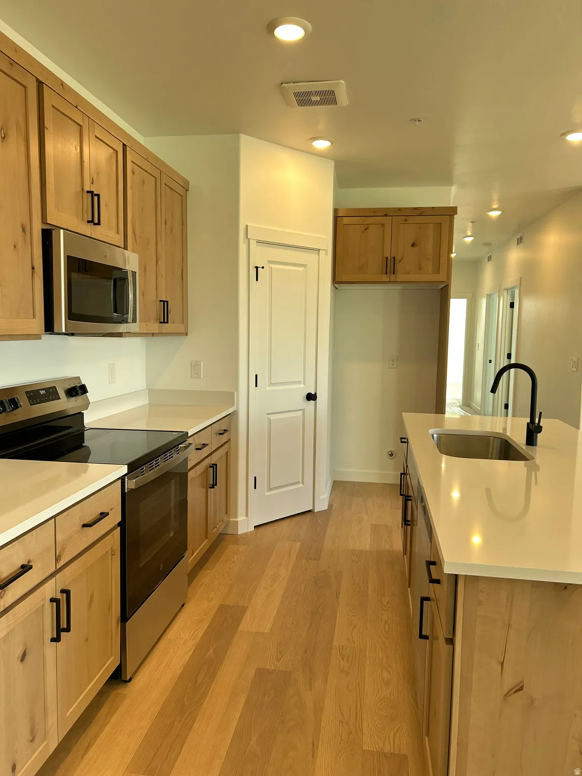 Kitchen featuring wood cabinetry, stainless steel appliances, light countertops, wood-finish flooring, and recessed lighting