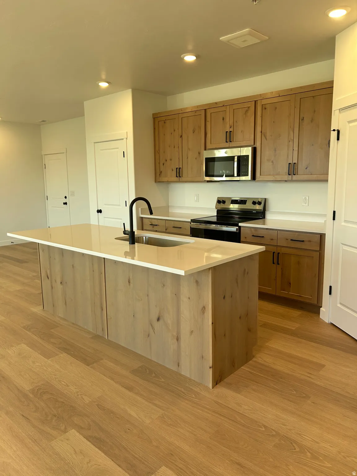 Kitchen featuring wood-finish flooring, an island with countertop and sink, natural wood cabinetry, stainless steel appliances, and recessed lighting