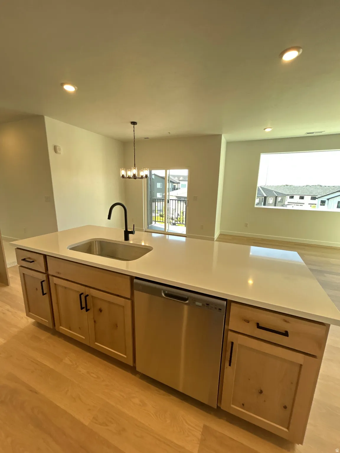 Kitchen island with light-toned countertop, stainless steel sink, black faucet, integrated dishwasher, and wood-finish cabinetry