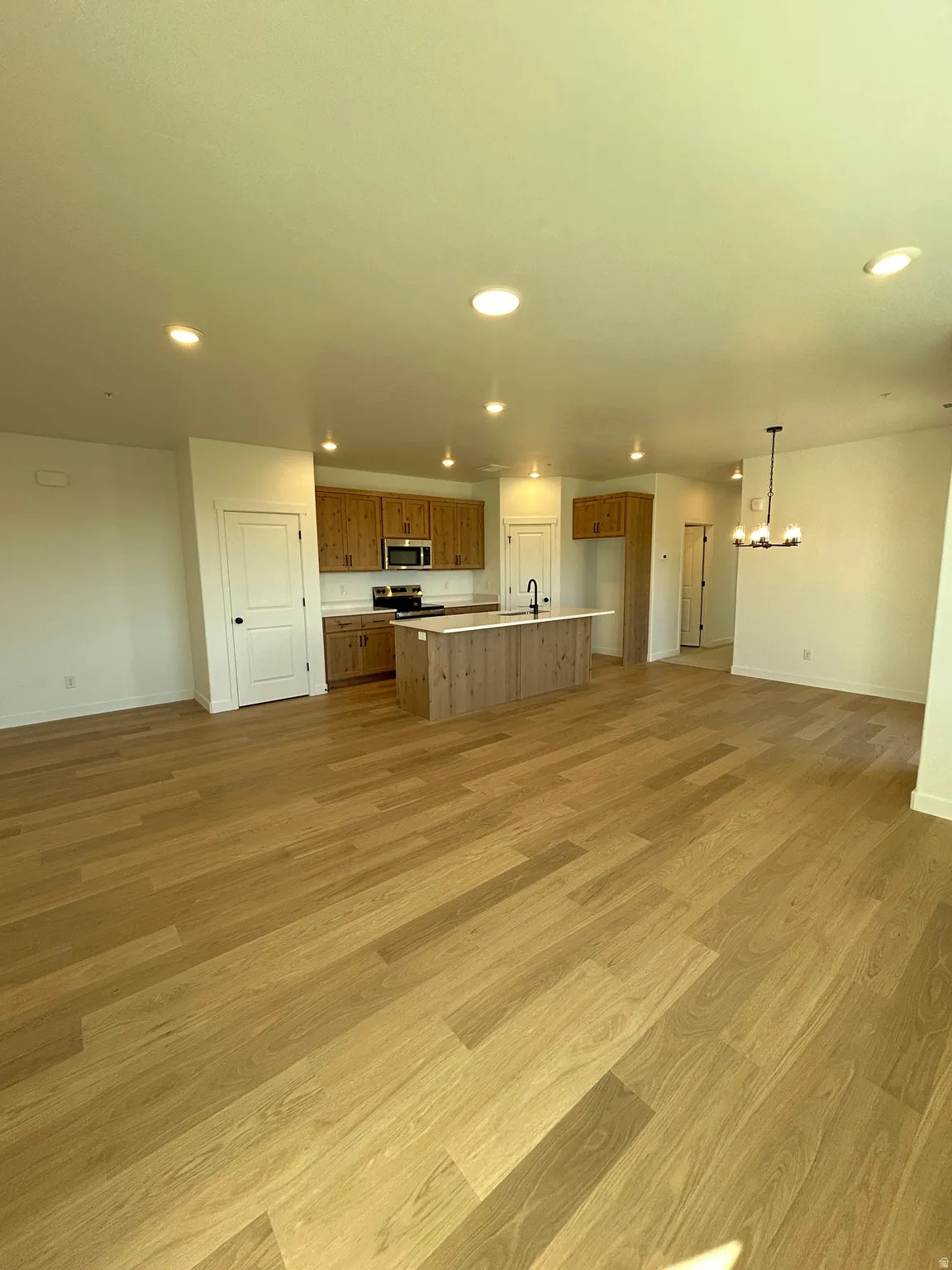 Open-concept kitchen and living area featuring wood-finish flooring, recessed lighting, and a kitchen island with a built-in sink