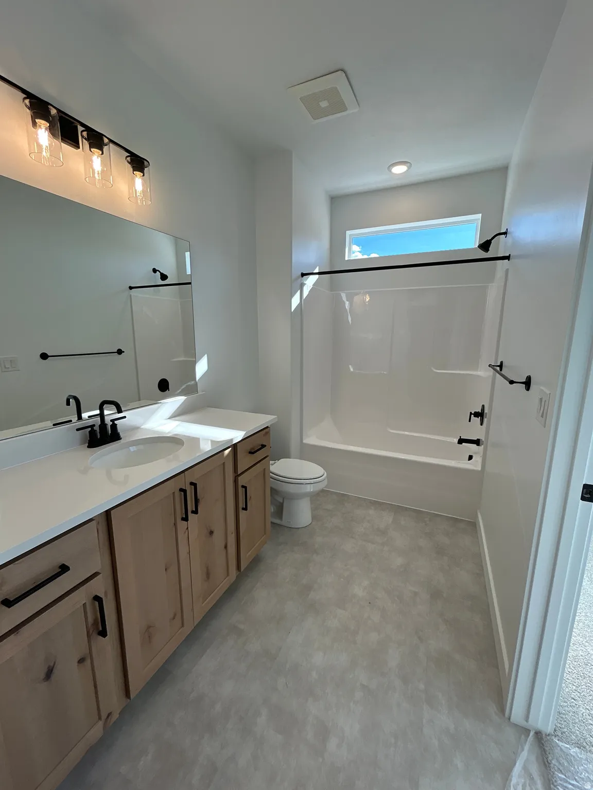 Dual basin vanity with white countertop, light wood-finish cabinetry, and black hardware