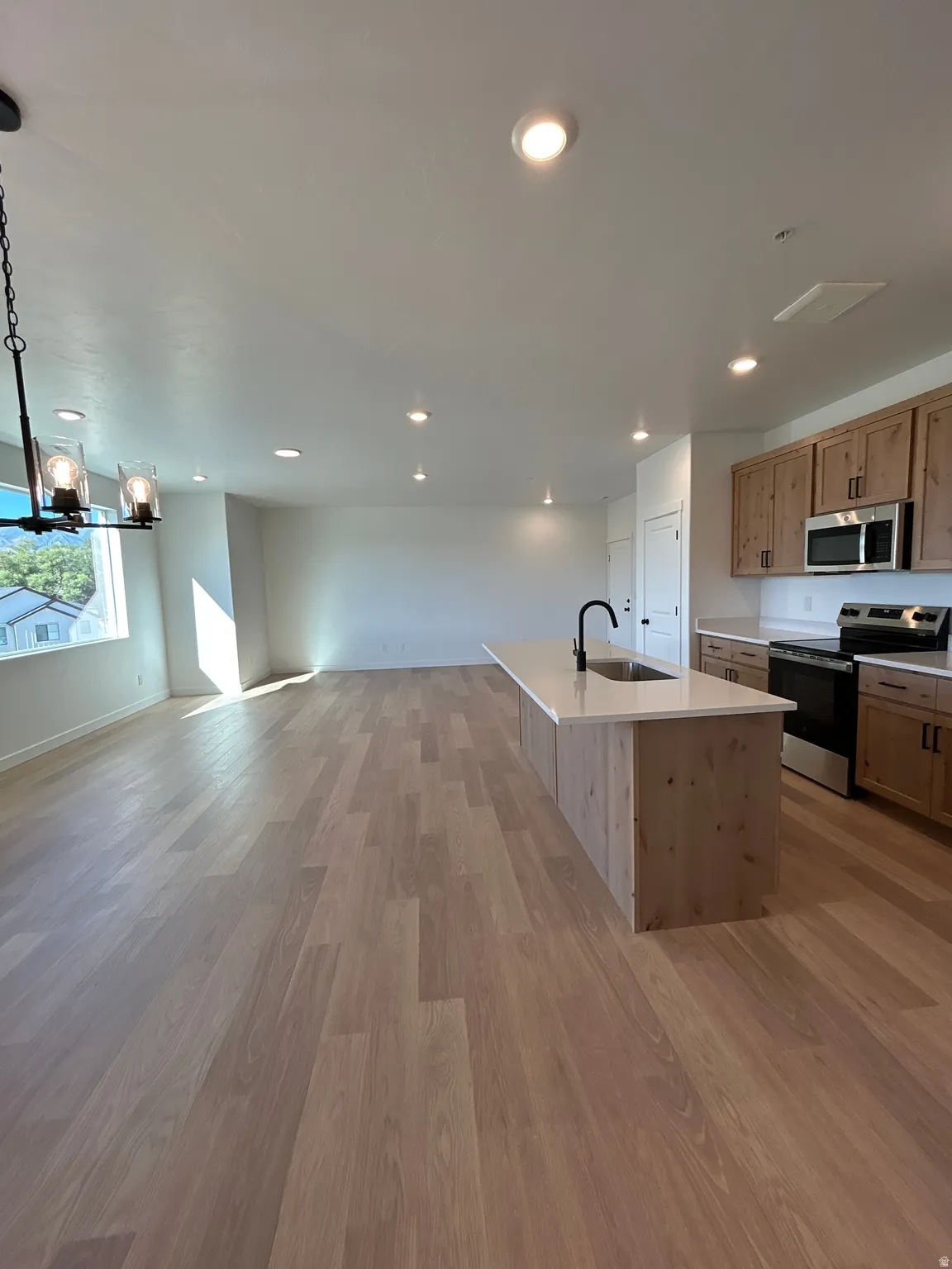 Open-concept living area featuring wood-finish flooring, recessed lighting, and a kitchen island with an integrated sink and light-toned countertop