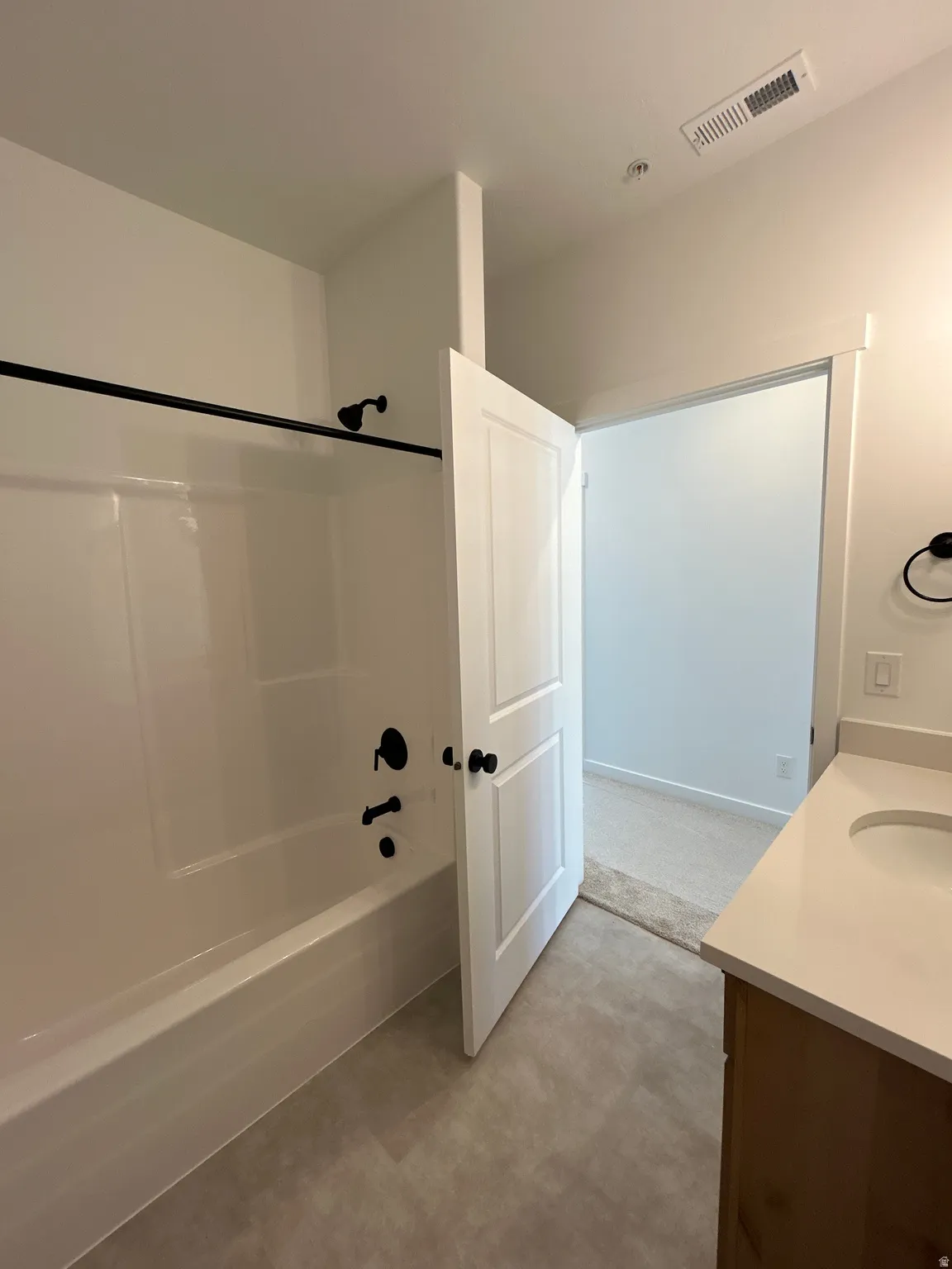 White bathtub with matte black fixtures, wood-finish vanity with an undermount sink, and light-toned countertop