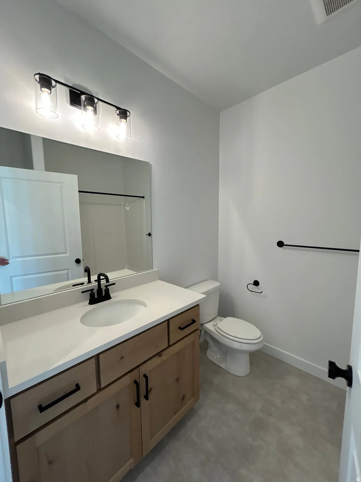 Wood-finish vanity with a white countertop and undermount sink, matte black faucet, and coordinating hardware