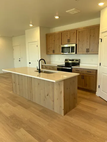 Kitchen featuring wood-finish flooring, an island with countertop and sink, natural wood cabinetry, stainless steel appliances, and recessed lighting