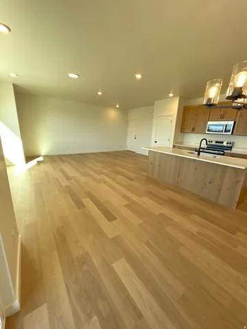 Open-concept living space with wood-finish flooring, recessed lighting, a kitchen island with a sink, stainless steel appliances, and a modern chandelier