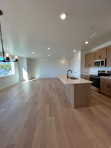 Open-concept living area featuring wood-finish flooring, recessed lighting, and a kitchen island with an integrated sink and light-toned countertop