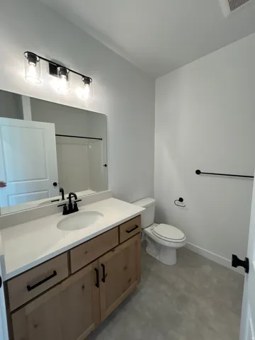 Wood-finish vanity with a white countertop and undermount sink, matte black faucet, and coordinating hardware