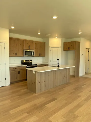 Kitchen featuring wood-finish cabinetry, stainless steel appliances, a center island with sink, light-toned countertops, and recessed lighting