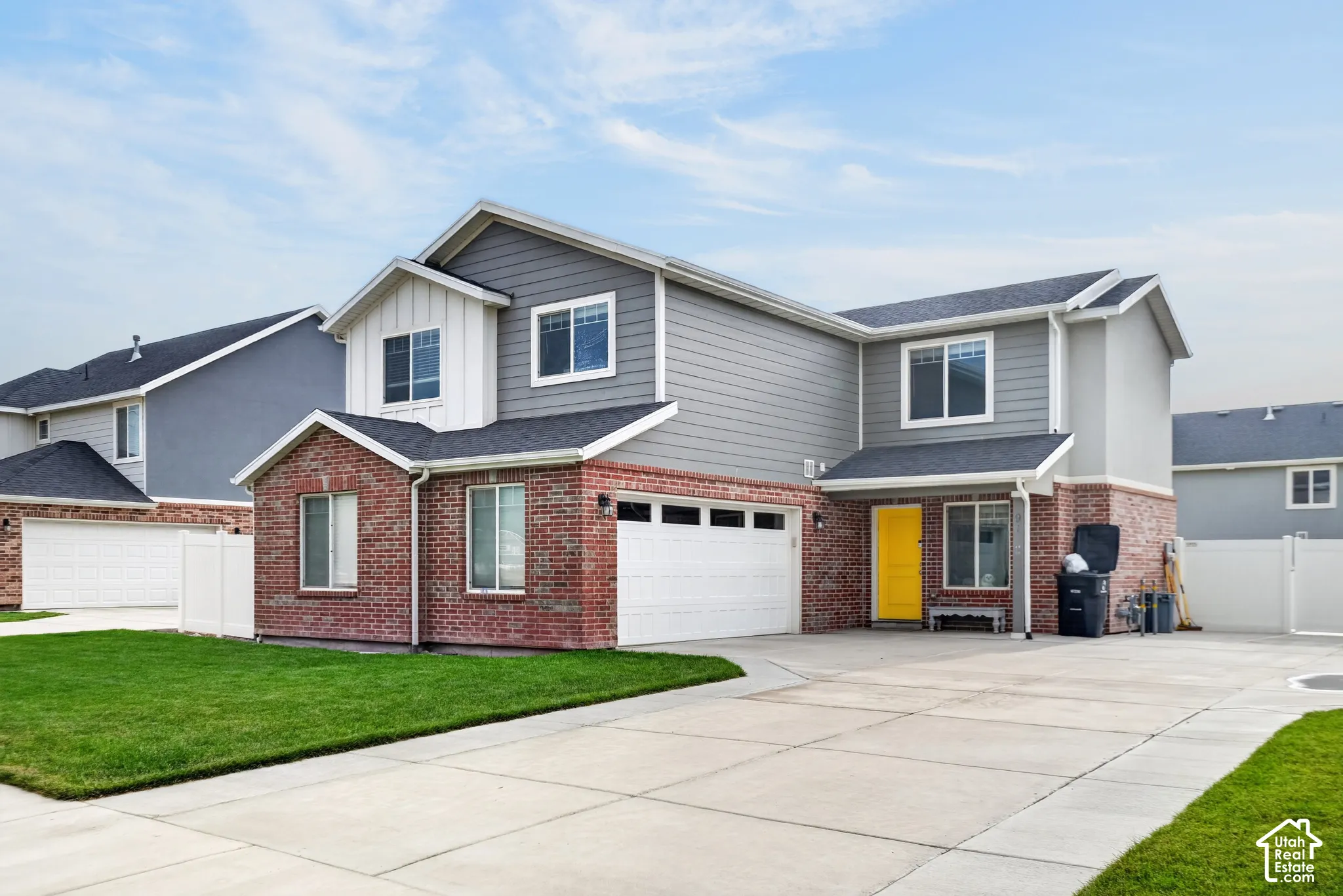Contemporary exterior featuring brick and horizontal siding, an attached two-car garage, a concrete driveway, a manicured lawn, and a white picket fence