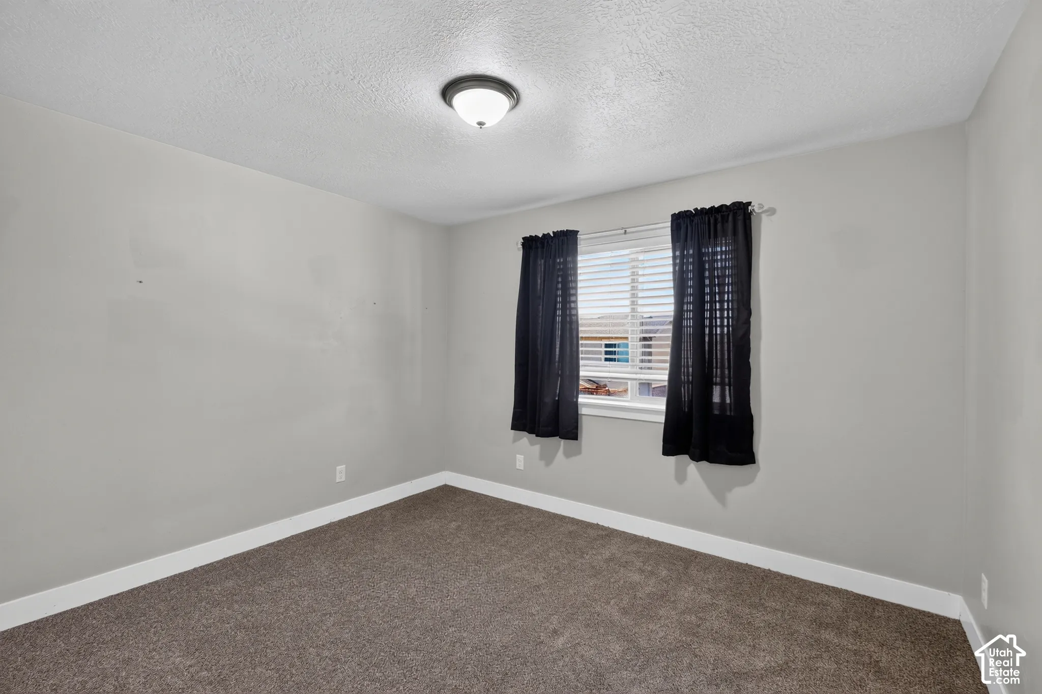 Neutral wall tones, carpeted flooring, and a window with horizontal blinds and an overhead flush-mount light fixture