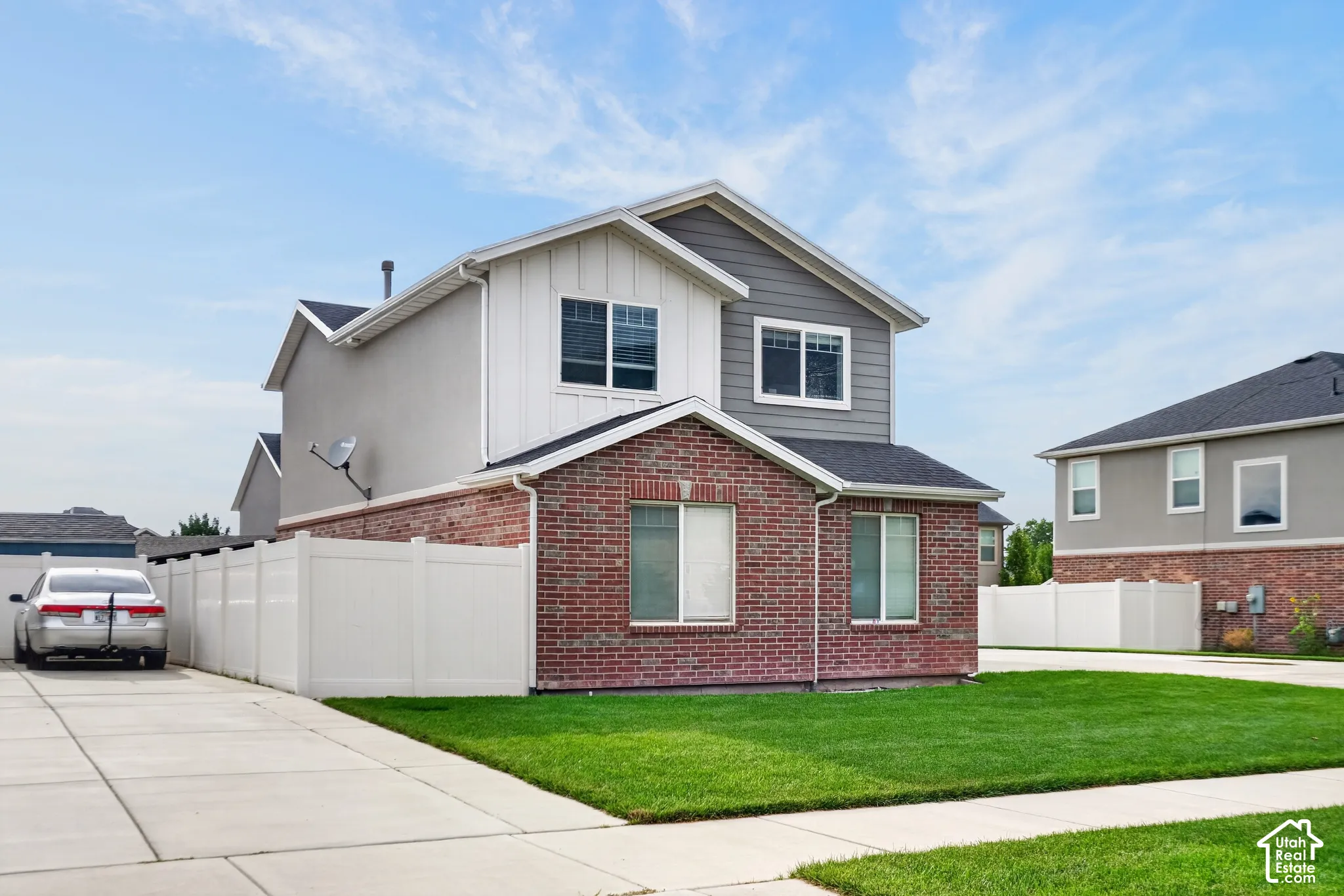 Brick facade, white vinyl fencing, concrete driveway, manicured lawn, and multiple windows