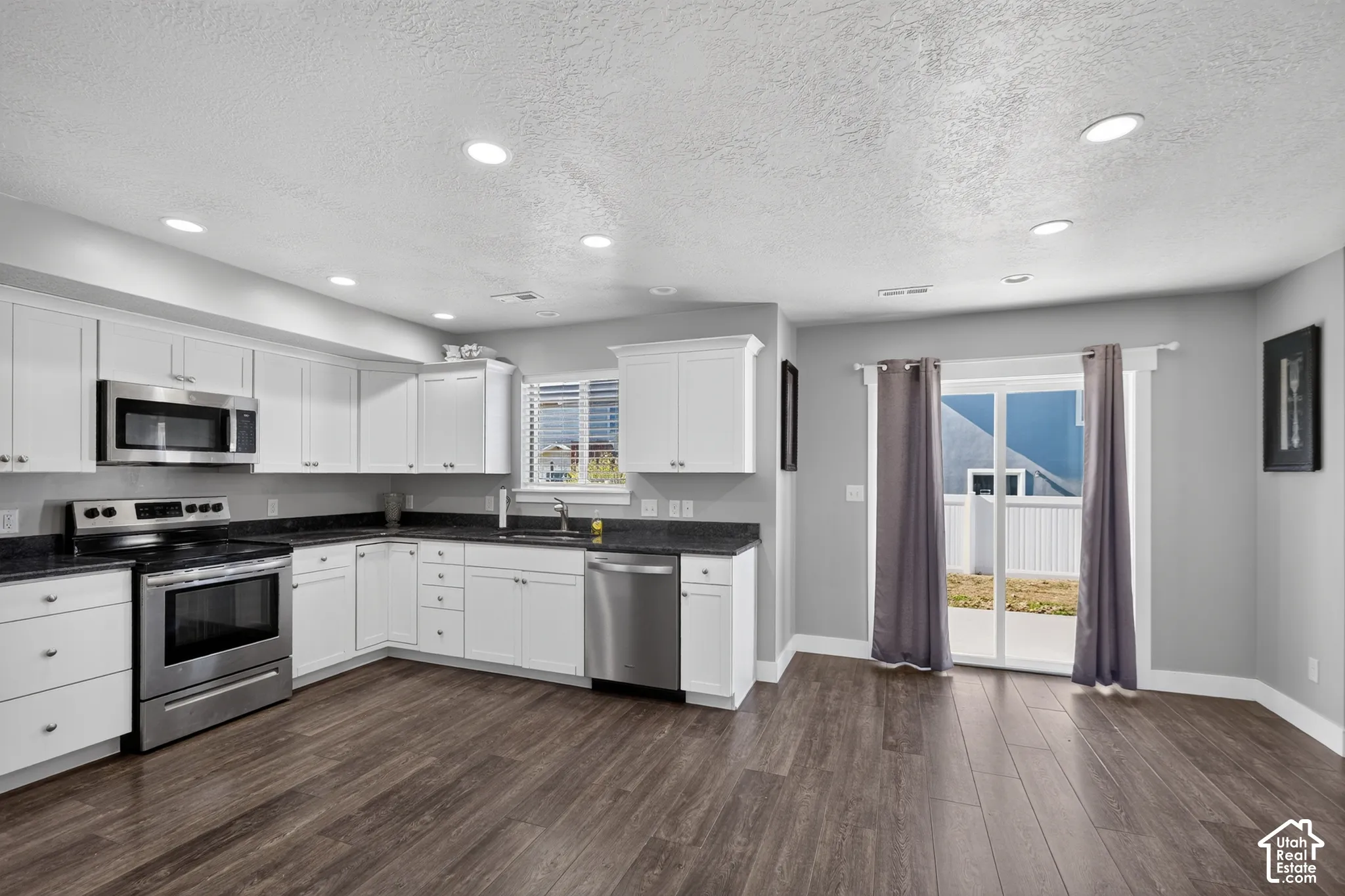 Kitchen featuring white cabinetry, dark stone countertops, stainless steel appliances, wood-finish flooring, and sliding glass doors