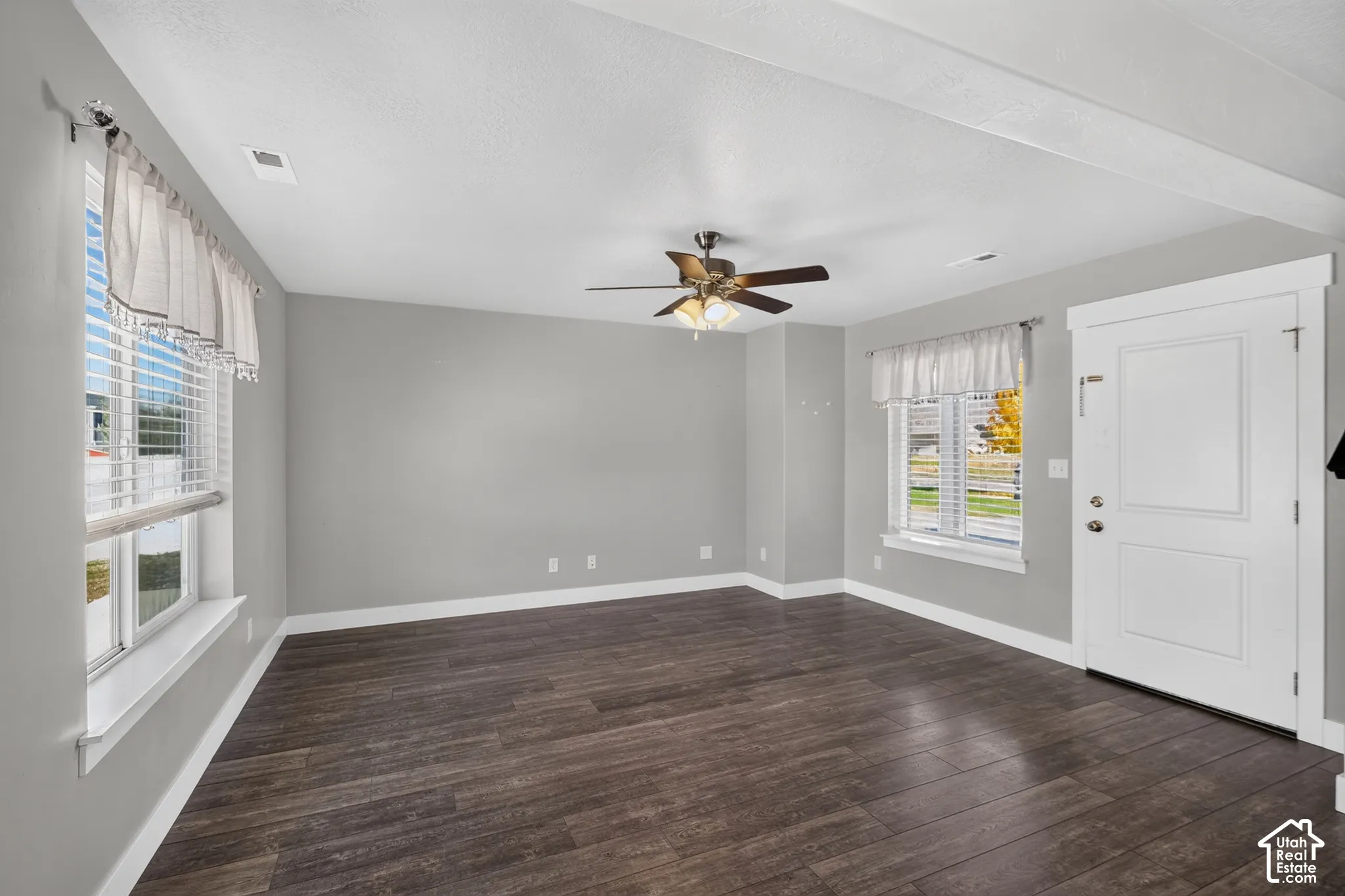 Living area featuring wood-finish flooring, neutral wall paint, multi-pane windows with integrated sills, and a centrally mounted ceiling fan with integrated lighting