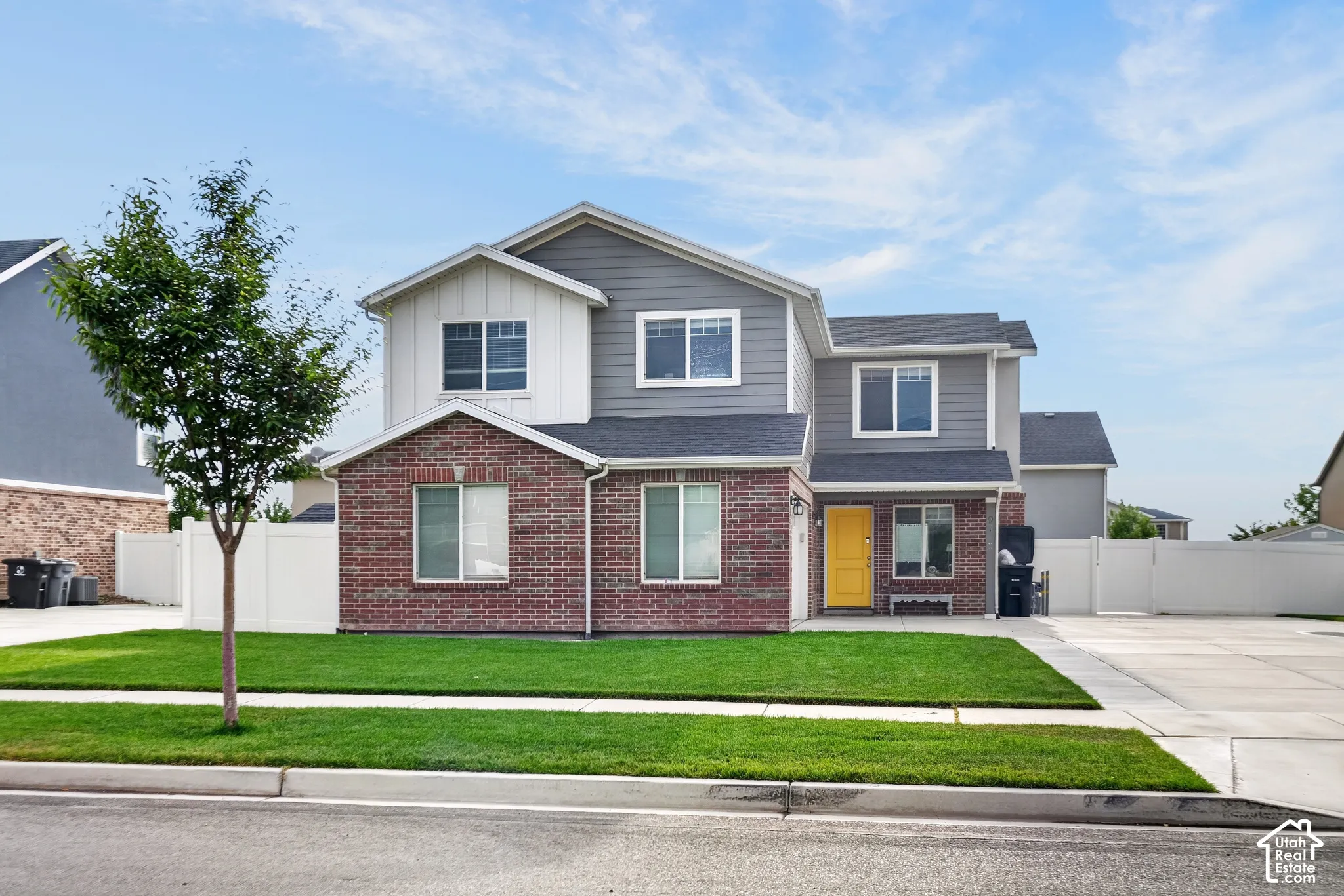 Two-story residence featuring brick and siding facade, a vibrant yellow front door, and a manicured front lawn