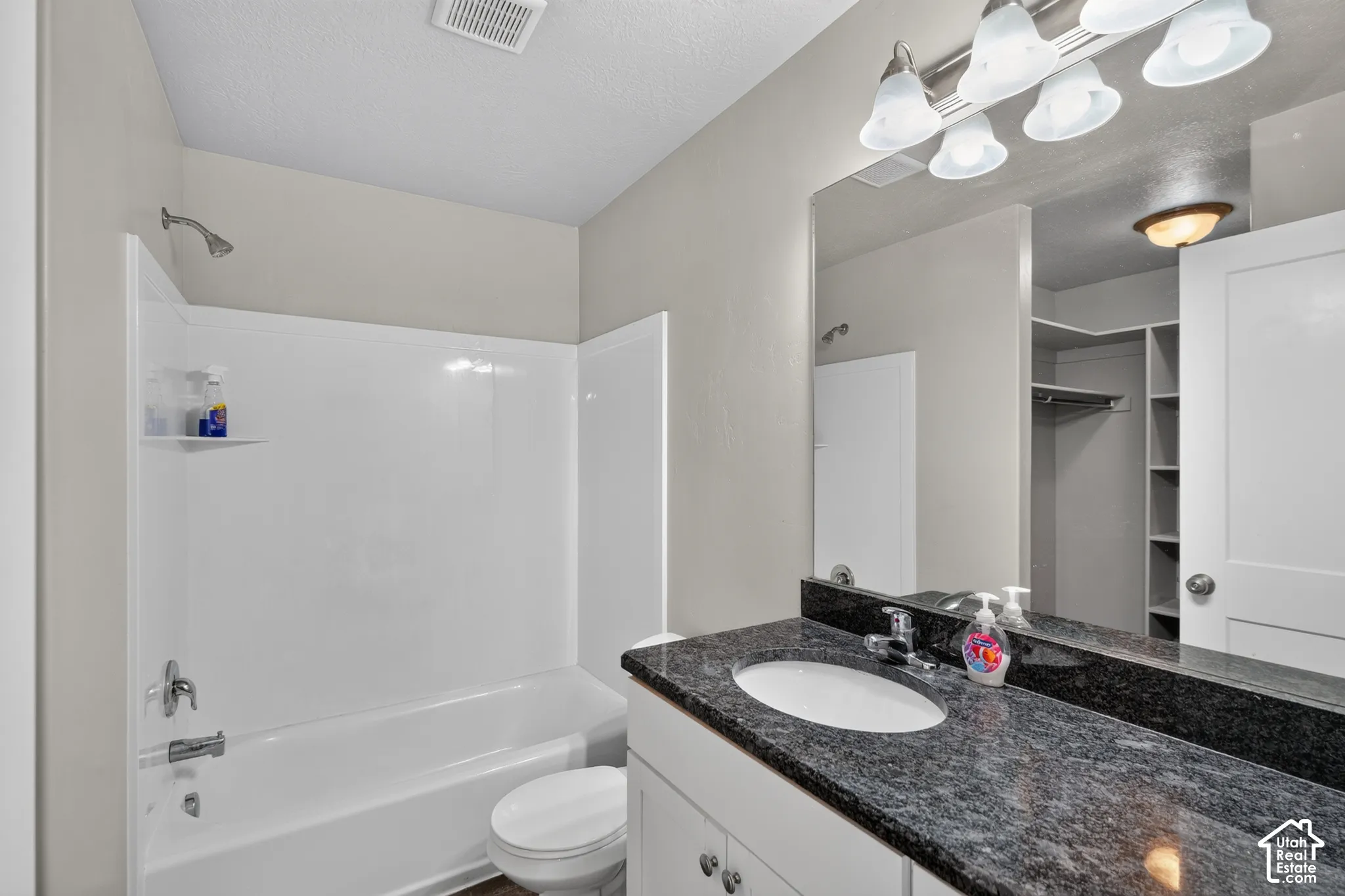 Full bathroom featuring a white vanity with a dark stone countertop, undermount sink, large wall-mounted mirror, four-light vanity fixture, and a white acrylic shower-tub combination