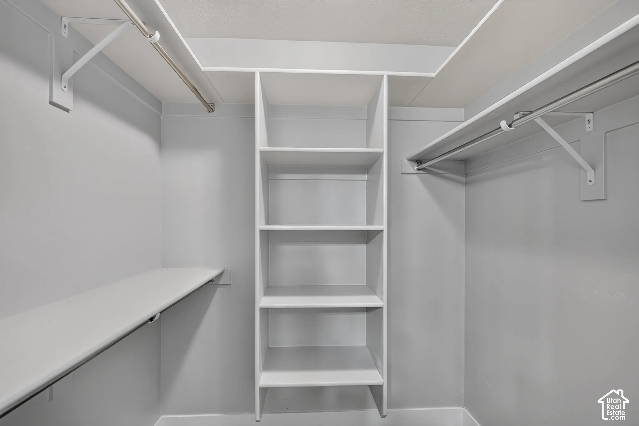 Walk-in closet featuring white built-in shelving, dual hanging rods, and overhead storage ledges