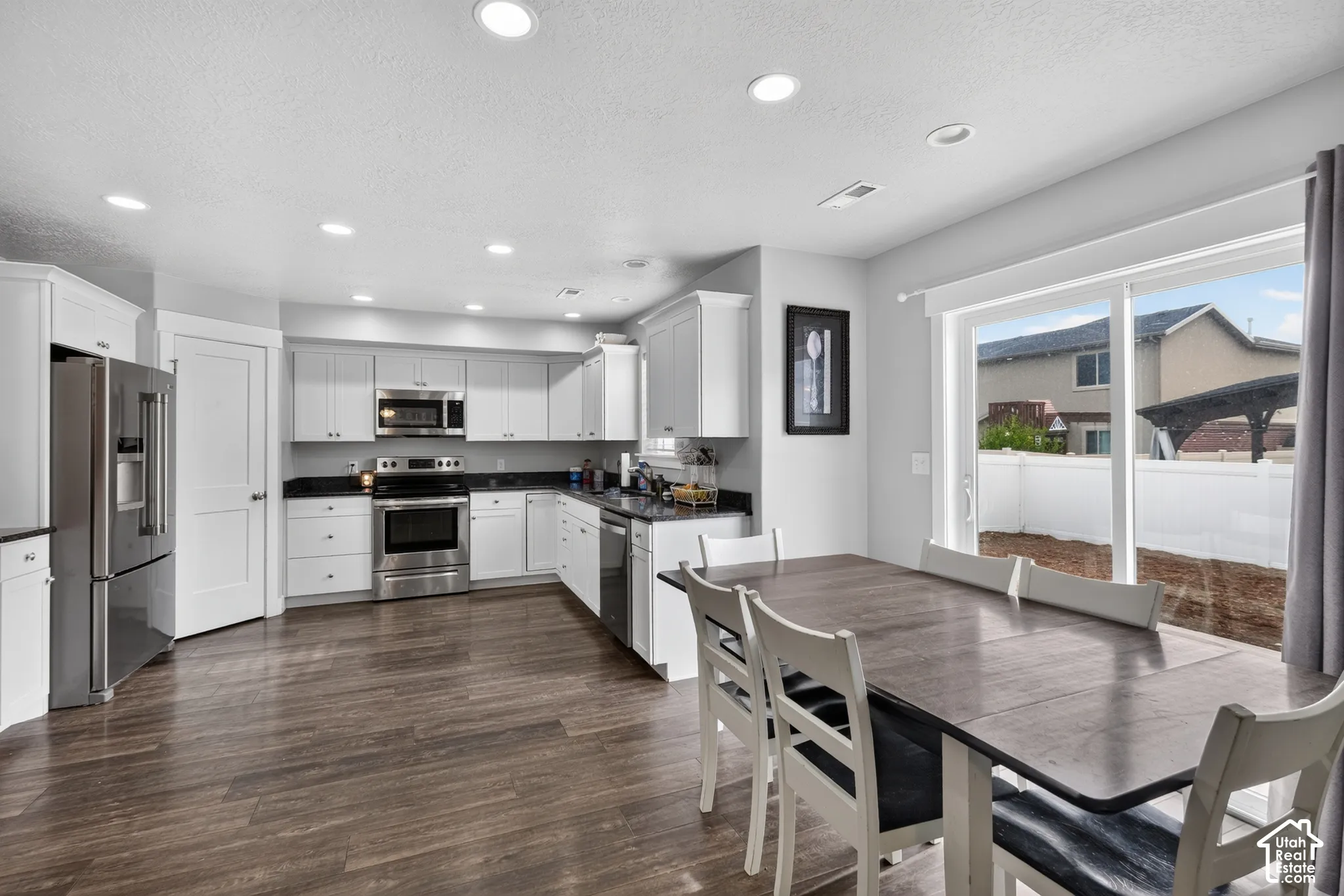Modern kitchen featuring white cabinetry, dark countertops, stainless steel appliances, and wood-finish flooring