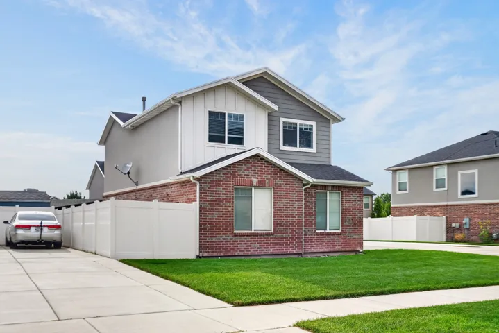 Brick facade, white vinyl fencing, concrete driveway, manicured lawn, and multiple windows