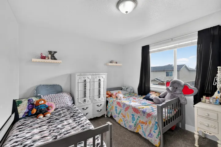 Recessed ceiling light fixture, window with black curtain panels, light gray carpet, white walls, and a built-in wall shelf