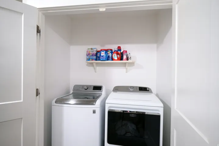 Built-in laundry closet featuring white panel doors, a top-loading washing machine, a front-loading dryer, and a wall-mounted storage shelf