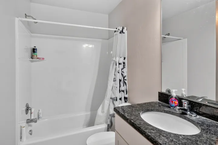 White bathtub with integrated shower, chrome fixtures, and a granite-finish vanity with an undermount sink