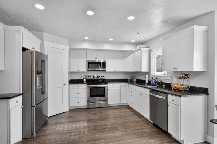 Kitchen featuring white cabinetry, dark stone countertops, stainless steel appliances, recessed lighting, and wood-finish flooring