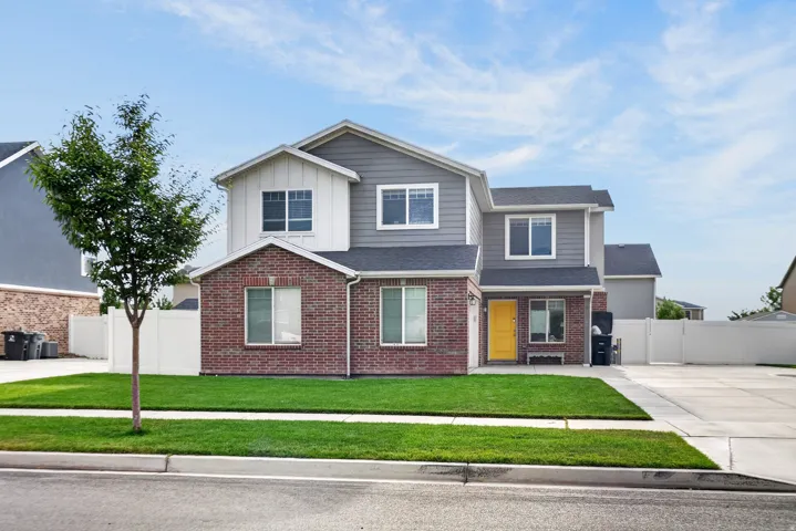 Two-story residence featuring brick and siding facade, a vibrant yellow front door, and a manicured front lawn