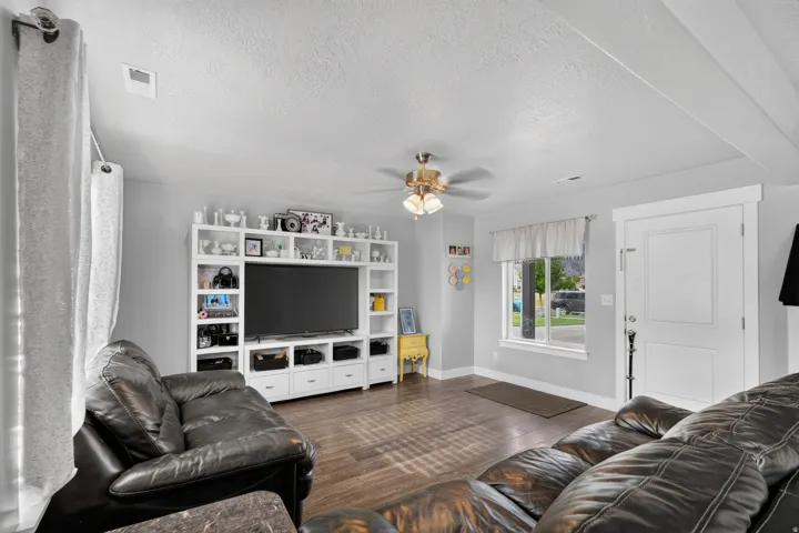 Built-in media center with open shelving, wood-finish flooring, ceiling fan with integrated lighting, and a white paneled door