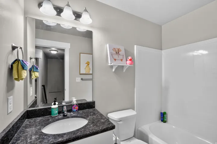 Vanity with dark countertop and undermount sink, wall-mounted mirror, and overhead light fixture