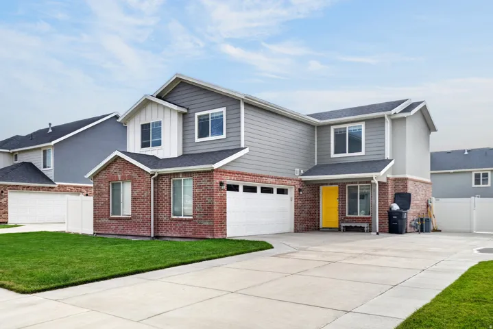 Contemporary exterior featuring brick and horizontal siding, an attached two-car garage, a concrete driveway, a manicured lawn, and a white picket fence