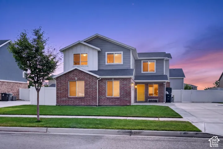Two-story exterior with a brick and siding facade, featuring a front lawn, paved driveway, and a white privacy fence