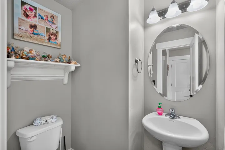Pedestal sink, wall-mounted oval mirror, three-light vanity fixture, and a white wall shelf