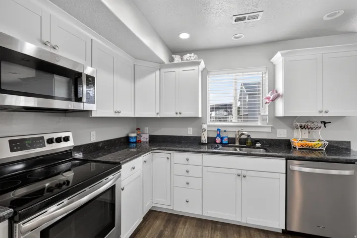 Kitchen featuring white cabinetry, dark stone-finish countertops, stainless steel appliances, and wood-finish flooring