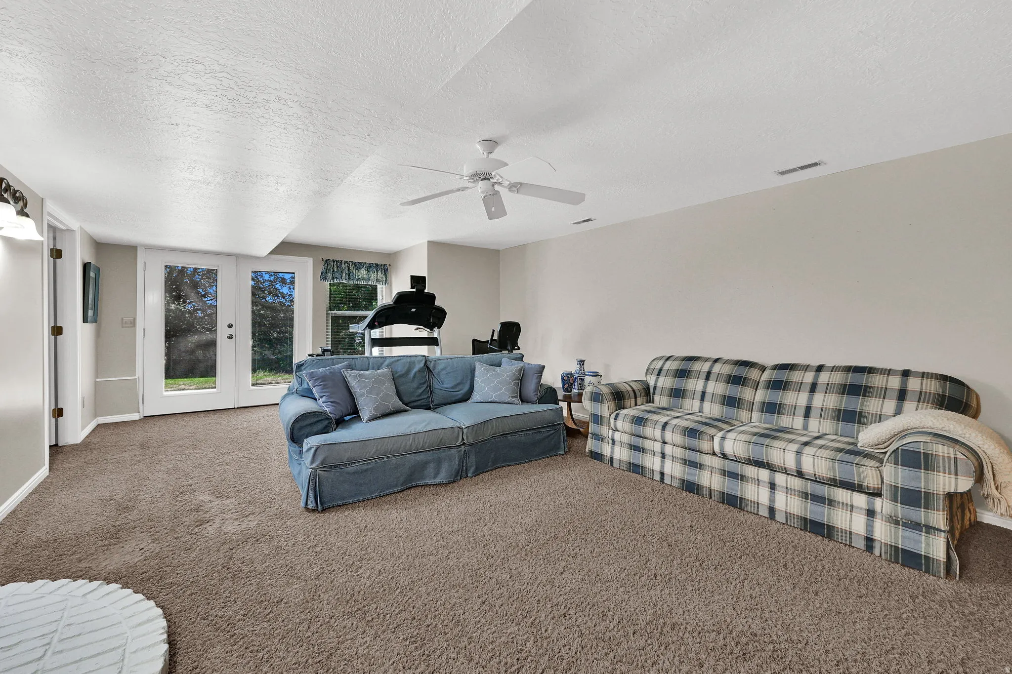 Spacious room featuring neutral wall tones, textured ceiling, carpeting, ceiling fan and double doors that walk out to the backyard.