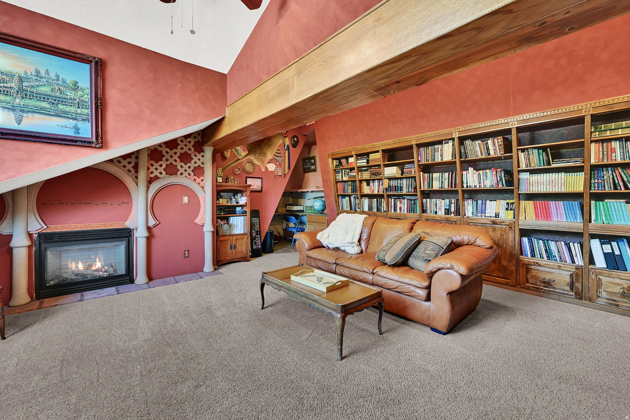 Built-in shelving, vaulted ceiling, exposed wood beams, gas fireplace, and carpet flooring.