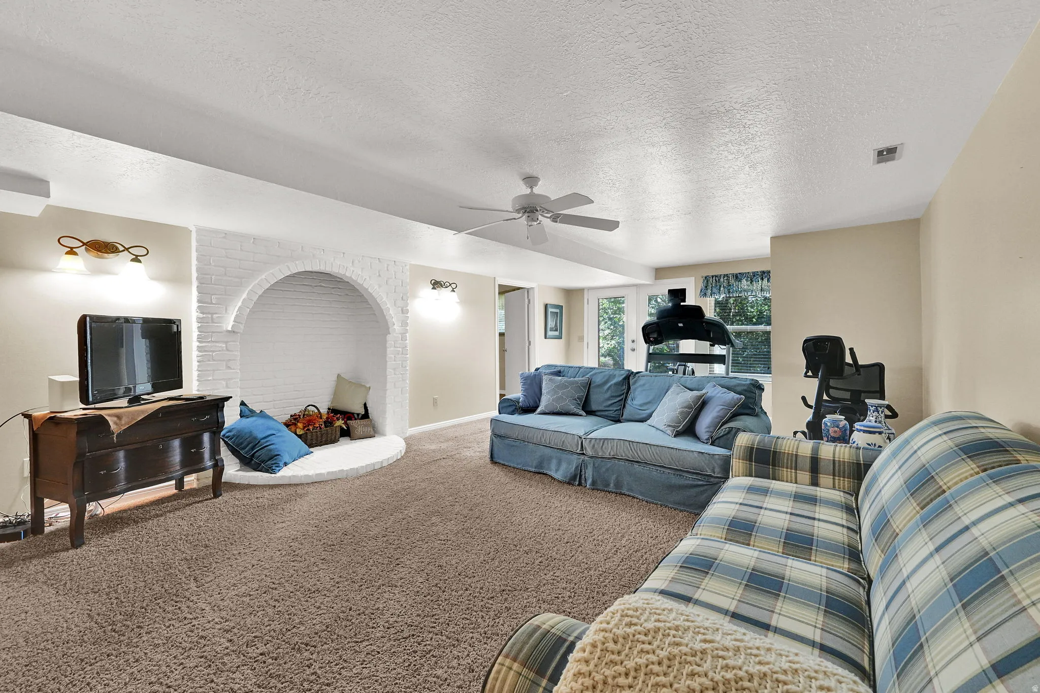 Expansive room featuring a white brick arched inset, wall sconces, a ceiling fan, and carpet flooring.