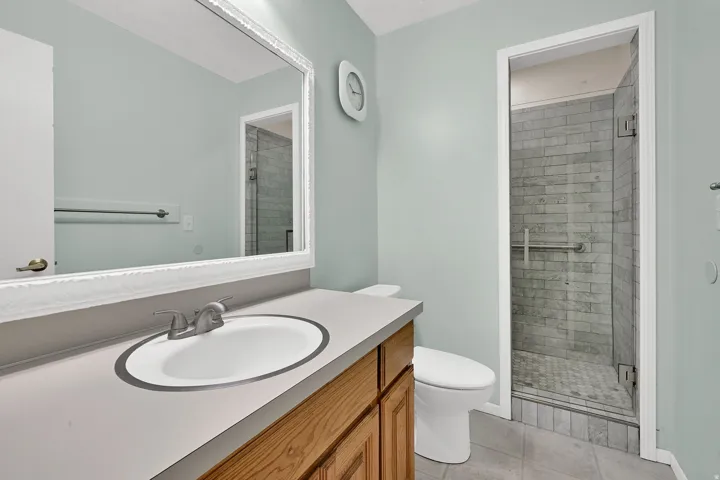 Bathroom featuring a wood-finish vanity with sink, a framed mirror, and a glass-enclosed shower with new tile.