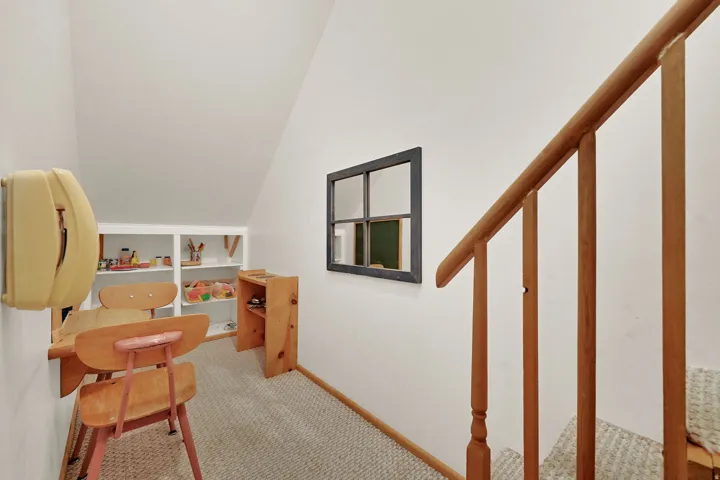 A kids playroom under the stairs with sloped ceiling featuring, built in shelving, a wall-mounted telephone, and wood staircase railing.
