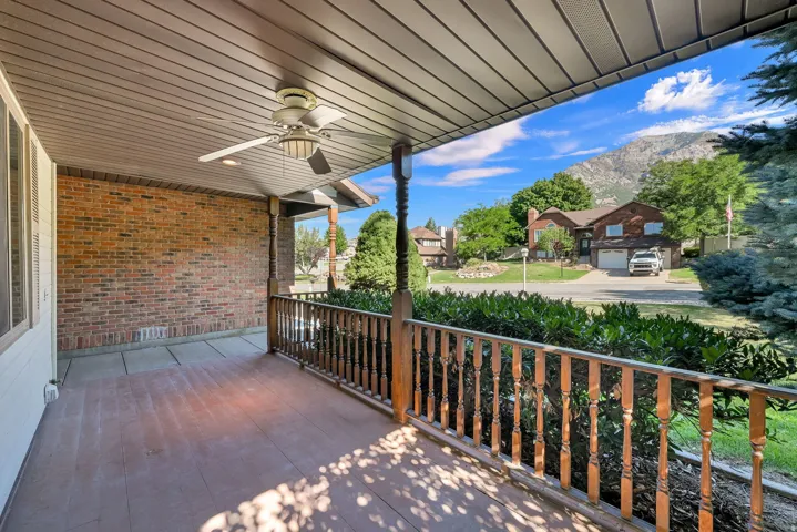 Covered front porch featuring a ceiling fan with light, brick exterior wall, and turned wood railing.