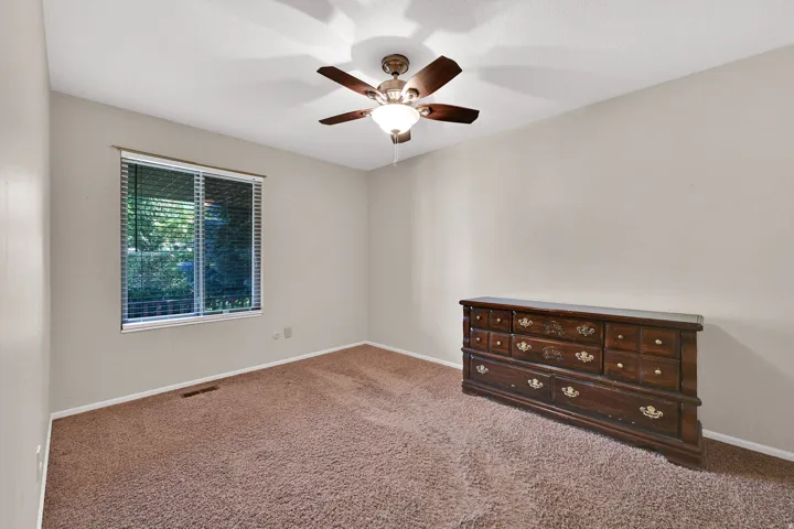 Second bedroom with neutral wall paint, textured ceiling, window with horizontal blinds, and a ceiling fan with integrated lighting.