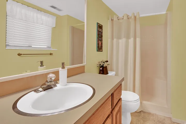 Vanity with sink, wood-finish cabinetry, neutral countertop, and a shower.