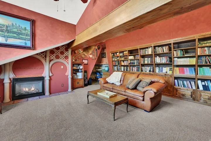 Built-in shelving, vaulted ceiling, exposed wood beams, gas fireplace, and carpet flooring.