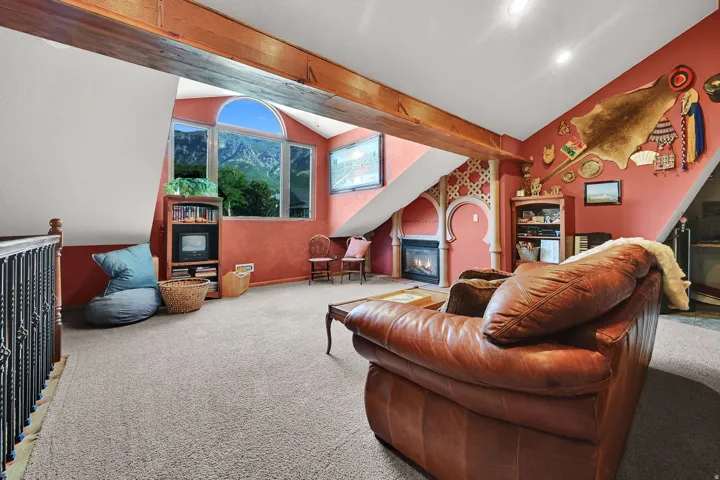 Arched picture window with mountain scenery, exposed wood beam ceiling, built-in gas fireplace, and recessed lighting.