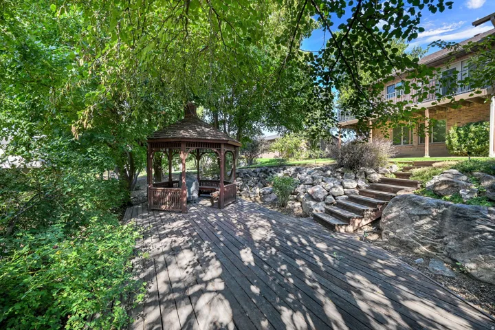 Expansive outdoor space featuring a wooden gazebo, a large wooden deck, natural stone retaining walls, and integrated wooden steps leading to the main structure.