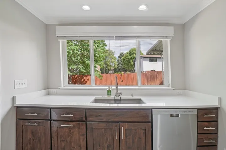 White countertops with a stainless steel sink, dark wood-finish cabinetry, and a stainless steel dishwasher