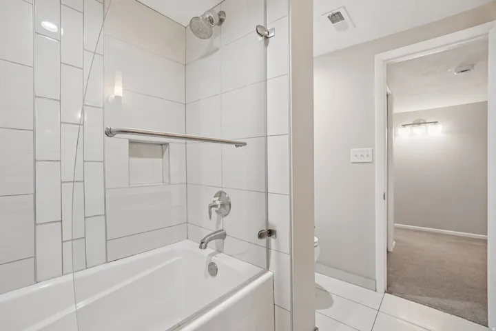 Bathtub with chrome fixtures, a rainfall showerhead, and a tiled shower surround with a built-in niche