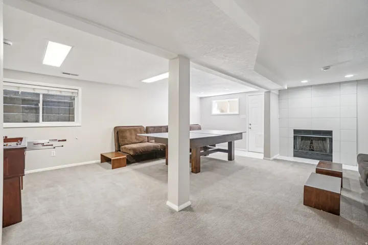 Recessed lighting, large rectangular windows, neutral carpeting, fireplace with tile surround, and a white paneled door