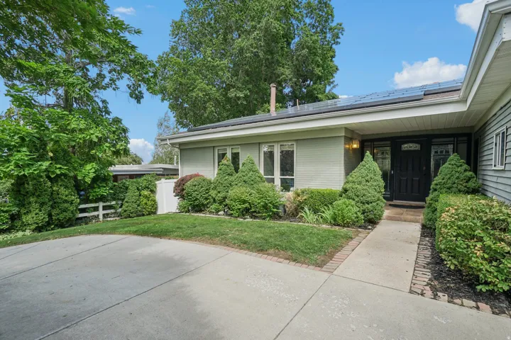 Manicured shrubbery and mature trees, concrete driveway, and a welcoming front entrance