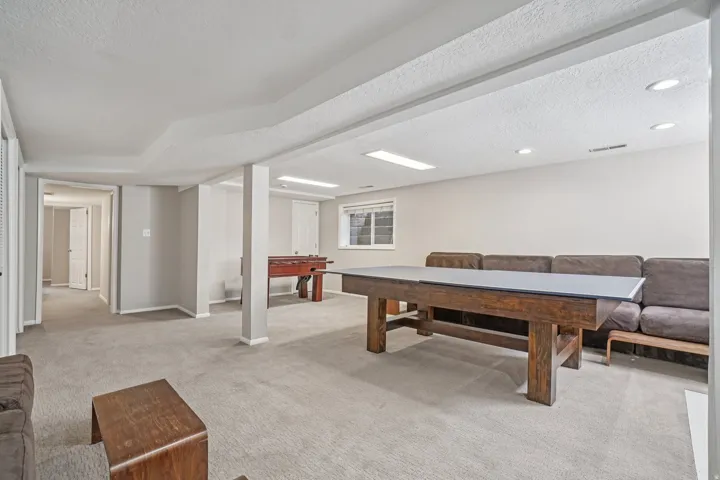 Expansive carpeted room with neutral wall tones, recessed lighting, and a window with white grilles